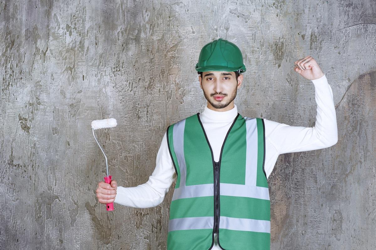 Engineer man in yellow uniform and helmet holding a trim roller for wall painting and showing positive hand sign. High quality photo. Essential Tips To Follow.