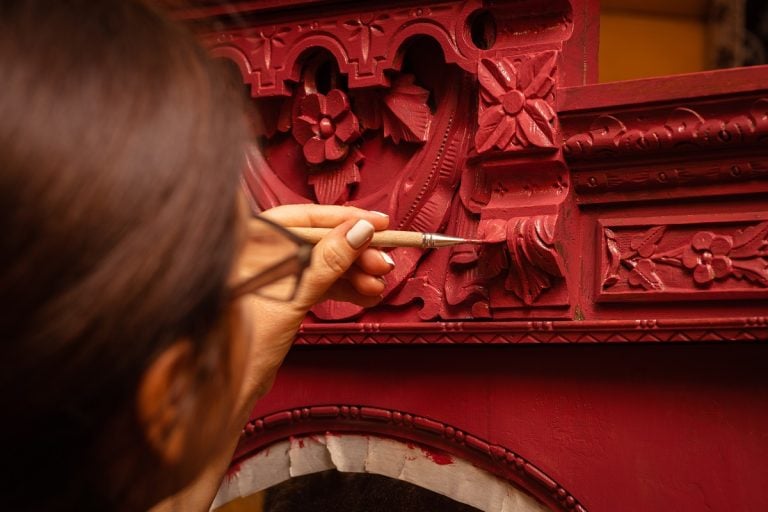 Closeup of female having thin brush in hand carefully painting old cupboard in red color. Home workshop for renovation of furniture. New life for old things. Paint For Antique Furniture.