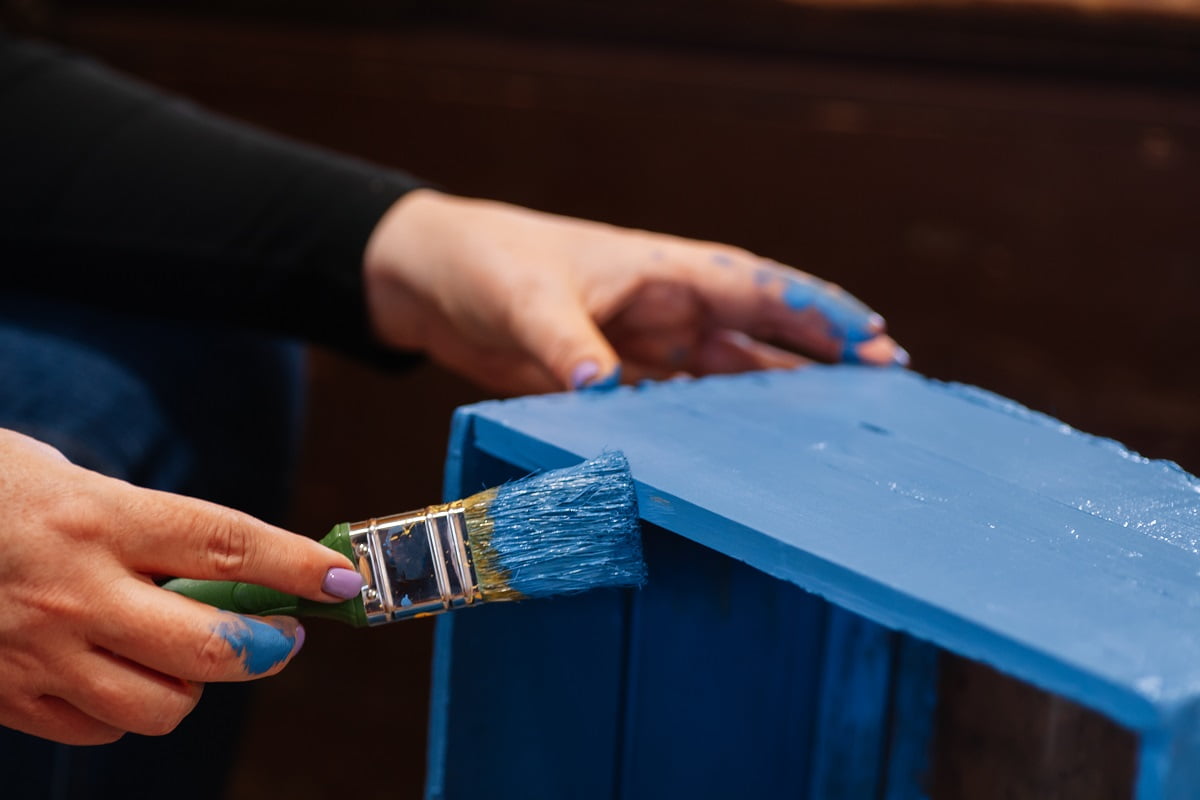 Closeup of big brush in stained hands coating closet drawer made of wood in blue color. Reuse of old things. Sustainable eco-friendly actions for planet future. Paint Techniques For Furniture Conclusion.