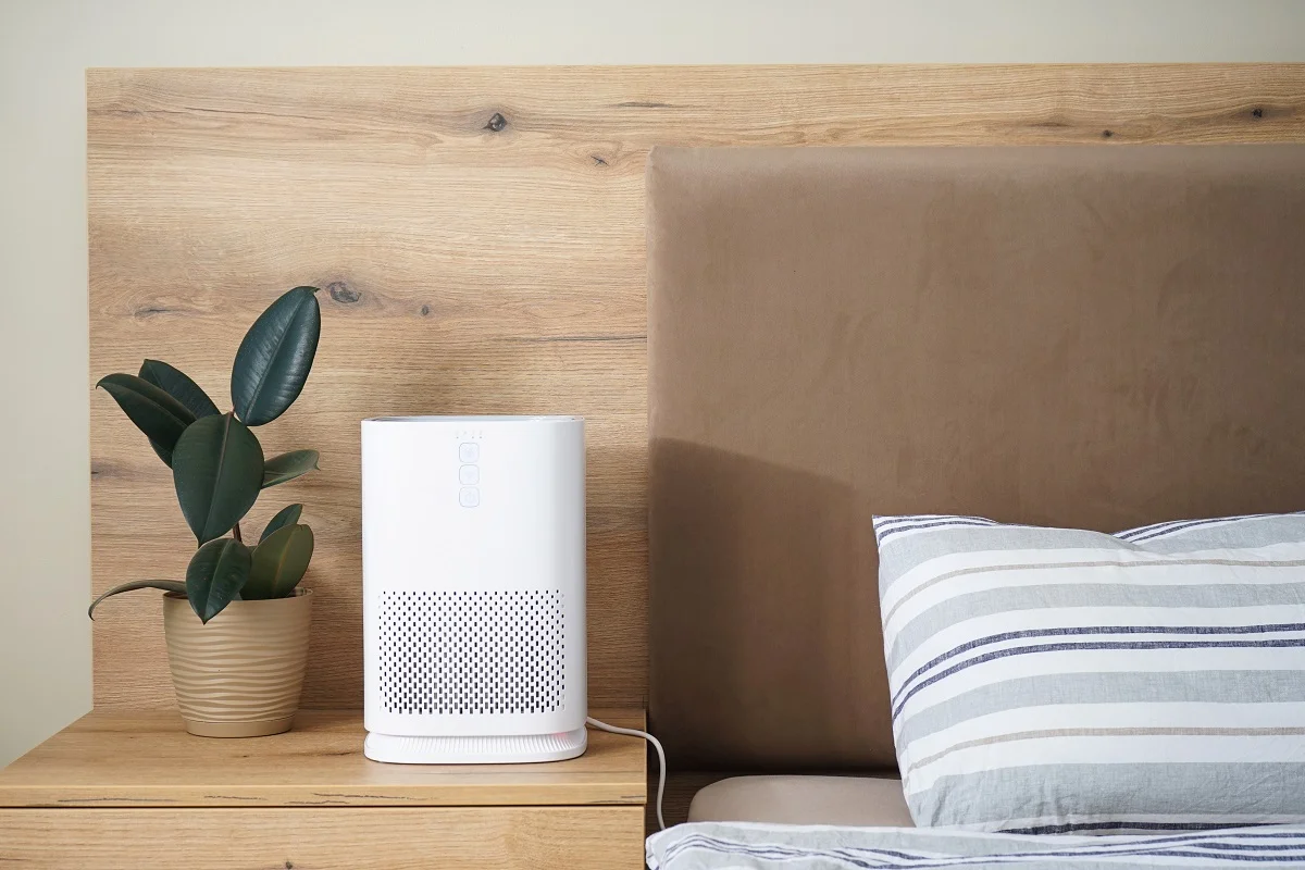 Modern air purifier in the bedroom by the bed, place for text. Benefits Of a Dehumidifier In Bedroom.