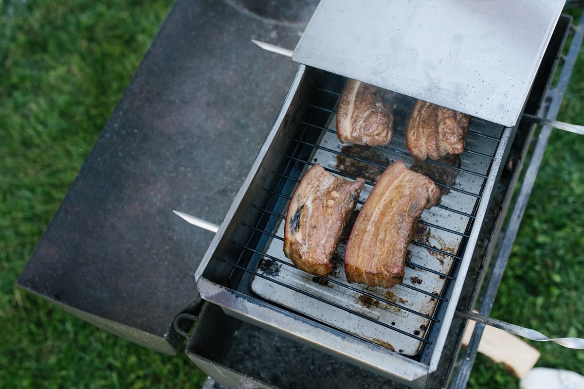 Bacon is smoked in a metal smokehouse in the open air. Insulated Smoker Buying Guide.