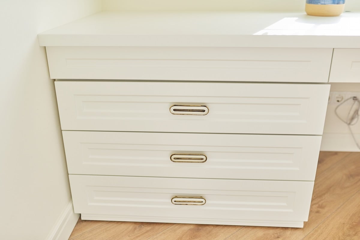 White wooden chest of drawers with vintage bronze handles under the desk in the interior of children's room, home office. Chalk Paint For Furniture Frequently Asked Questions.