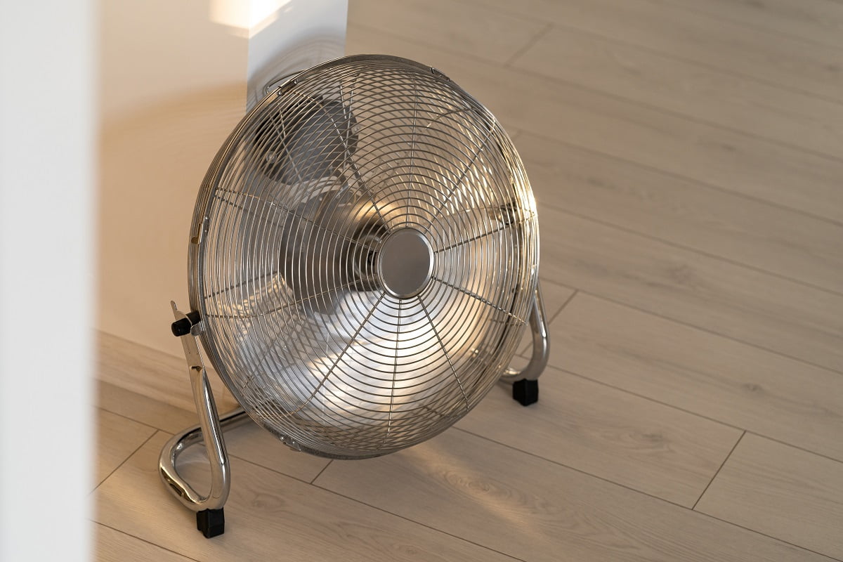 Silver metal ventilation fan on wooden floor at home. Lasko High Velocity Floor Fan.