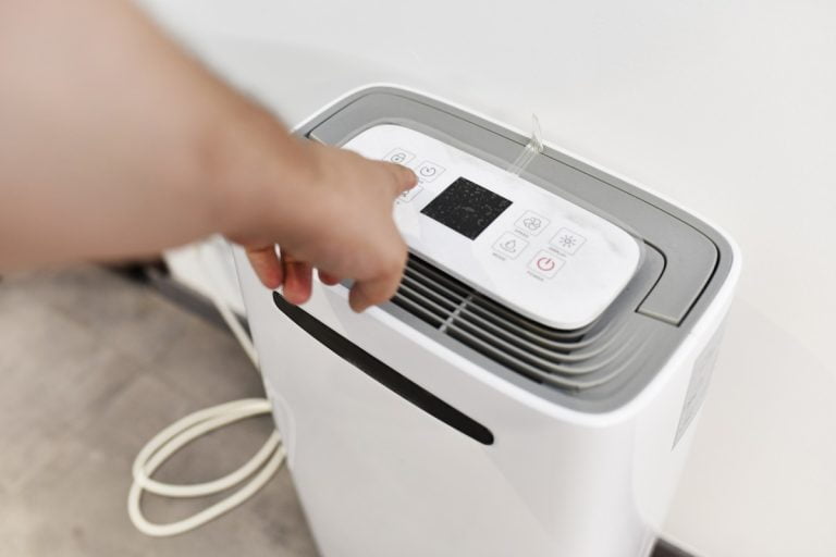 man's hand turning on a dehumidifier in the entrance of a house or office. To prevent joint pain. What Temperature Should I Set My Dehumidifier In Bedroom.