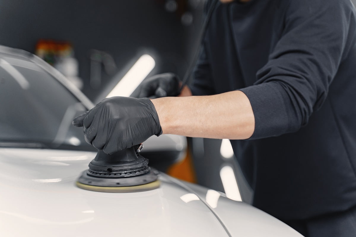 Man in a garage. Worker polish a car. Man in a black uniform. How Does An Angle Grinder Work.