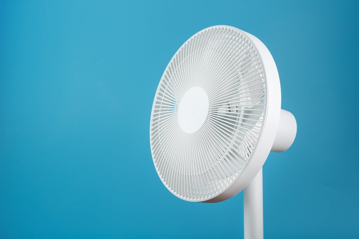 Electric fan in white with a modern design for cooling the room on a blue background. Free space, minimalistic style. Reasons Behind Fan Blowing Hot Air.