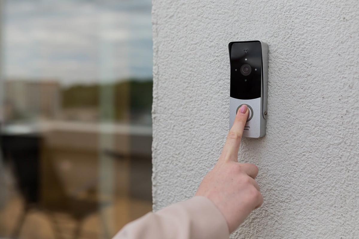 woman's hand uses a doorbell on the wall of the house with a surveillance camera. What Is A Wireless Doorbell.