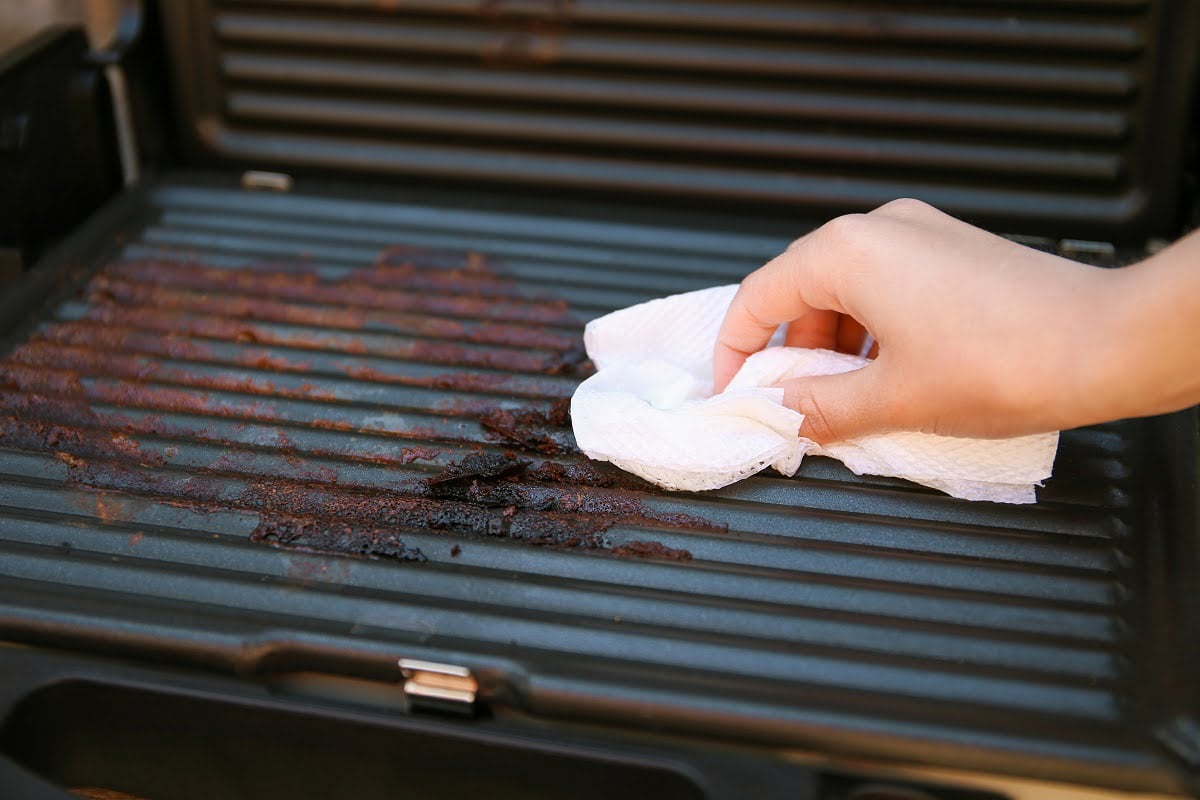 Dirty electric grill. Female hand wiping with cloth grill. Steps To Clean An Electric Smoker.