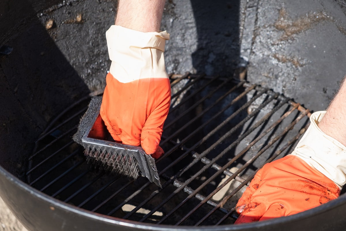 Male hand with red gloves cleans round grill with stiff brush. Cleaning A Pellet Smoker Grill.