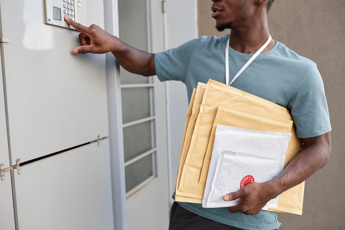Cropped shot of delivery worker ringing doorbell and holding packages. Wired Or Wireless- Which Doorbell Is Better.