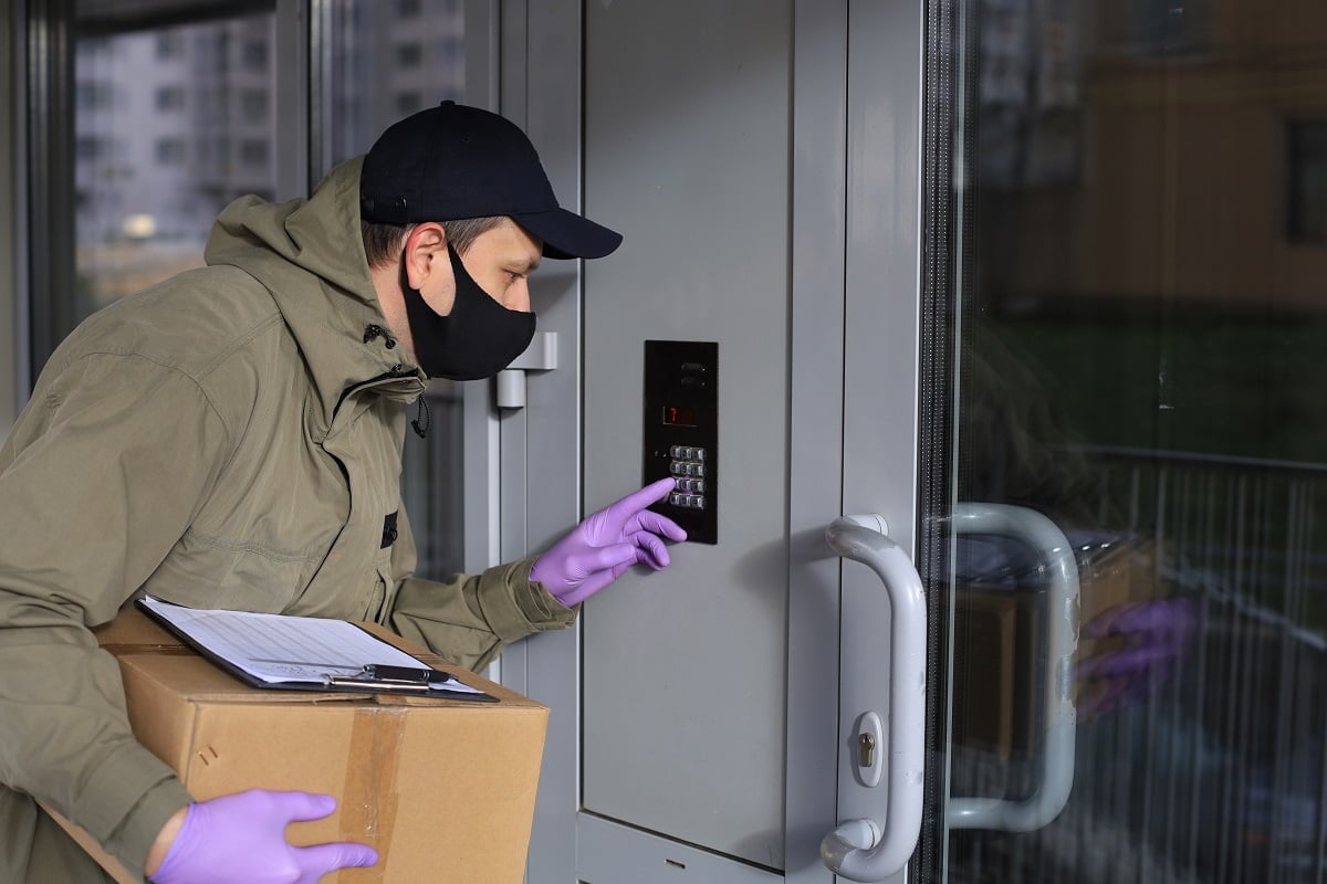 Courier in medicine mask and gloves with parcel calls the intercom to deliver the order to the customer. Coronavirus and quarattine concept. What Is An UPVC Frame.