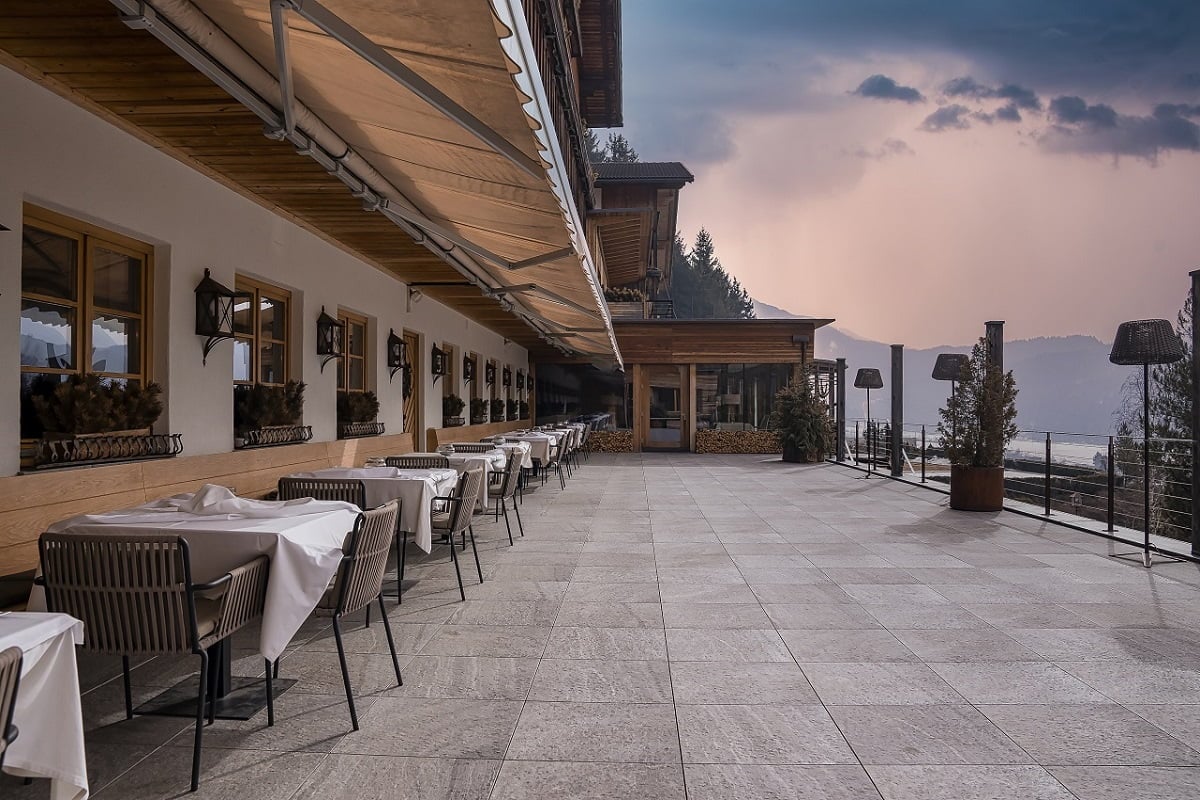 Tables and chairs arranged by windows. Beautiful outdoor place setting at restaurant against sky. Exterior of dining hall in luxurious ski resort during sunset. How To Retract A Power Awning.
