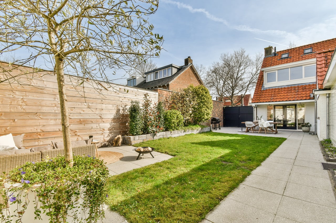 Neat paved patio with sitting area and small garden near wooden fence. Outdoor Privacy Screen Ideas You Should Try for Your Home.