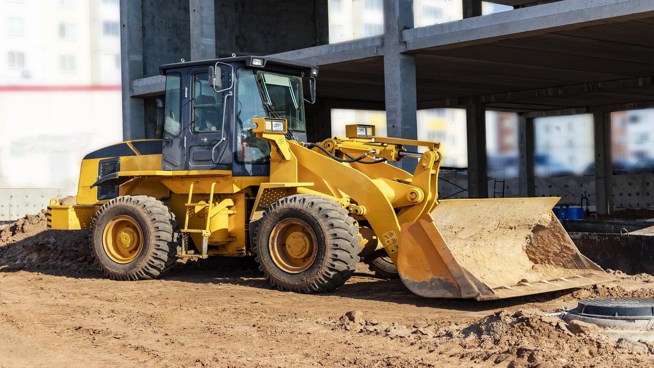 Heavy wheel loader with a bucket at a construction site. Close-up. Equipment for earthworks, transportation and loading of bulk materials - earth, sand, crushed stone. Wheel Loaders.