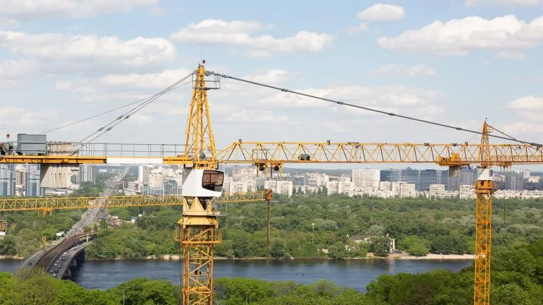 Residential building concept: yellow tower cranes at the construction of the low rise houses near the river and forest.Types Of Heavy Construction Equipment.