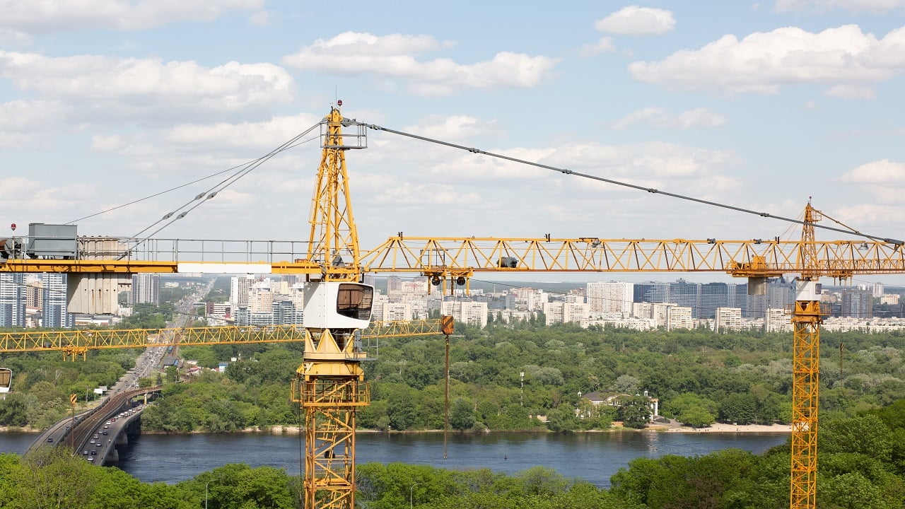 Residential building concept: yellow tower cranes at the construction of the low rise houses near the river and forest.Types Of Heavy Construction Equipment.