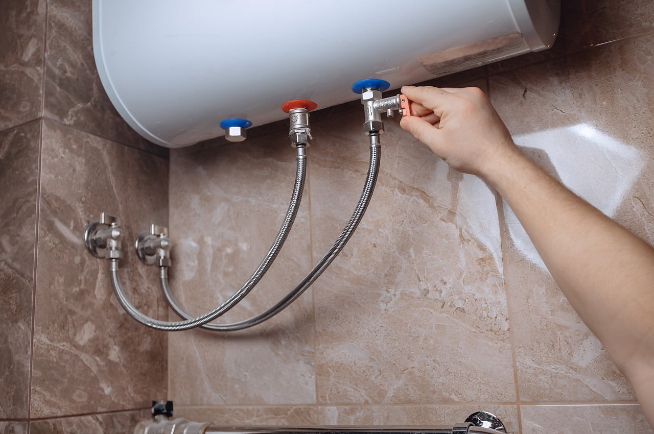 A man's hand adjusts the wall-mounted water heater in the bathroom. Turn the taps. Beige marble tiles.Best Water Heater Brands Conclusion