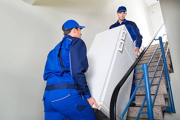 Side view of movers carrying refrigerator while climbing steps at home. Assemble Your Moving Equipment.